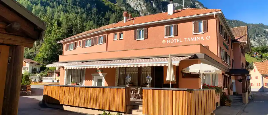 Hotel Tamina Frontansicht in hellem Orange und grosser Gartenterasse mit Holzzaun.